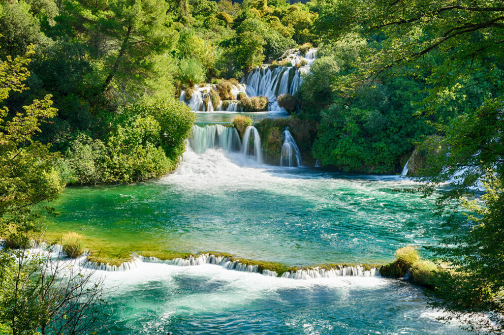 Cascading waterfalls surrounded by lush greenery in Krka National Park, Croatia, creating a picturesque and serene natural landscape.