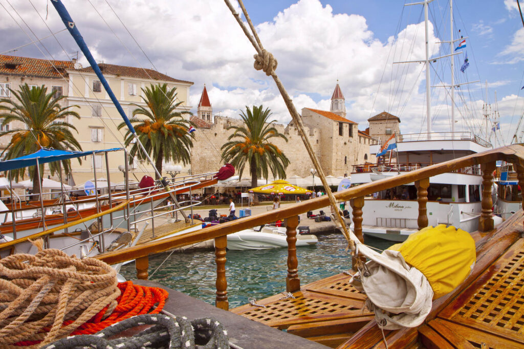 Boats peacefully lined along Trogir's seaside promenade, poised and ready for departure under the clear skies.